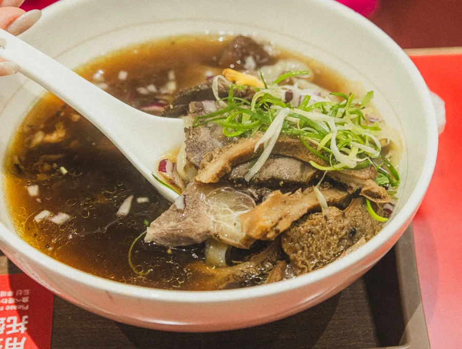 一碗暖色调牛肉汤面,撒有青葱